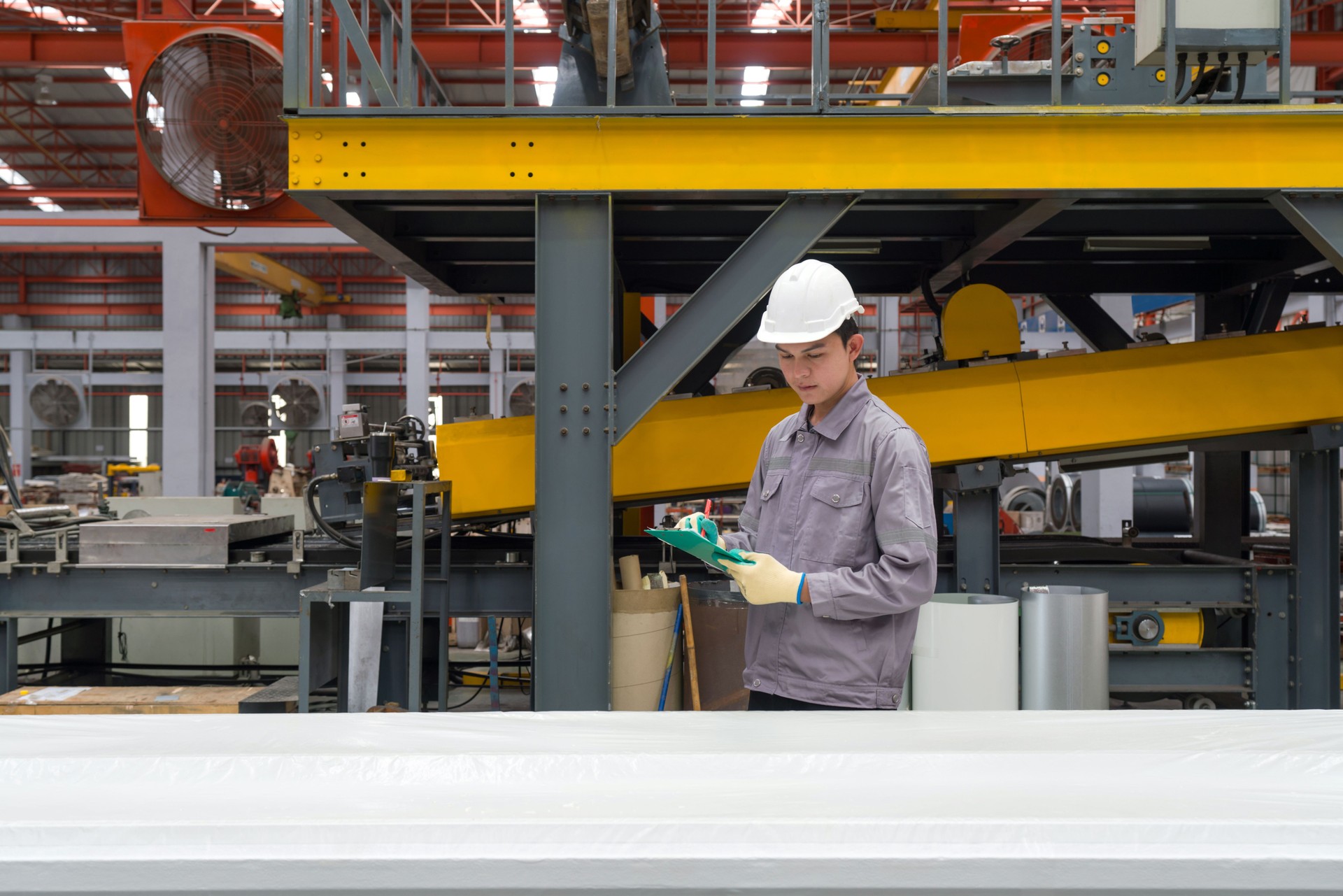 a worker check tasks while wearing a safety helmet and gloves, surrounded by machine and material. Work atmosphere in GreenLuck WPC manufactory.
